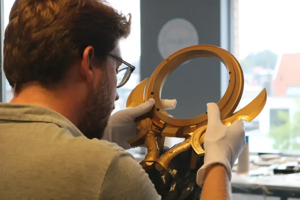 A Fabit craftsman inspecting a gold trophy component with white gloves in the workshop